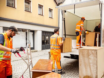 Mehrere Männer beladen einen LKW mit Möbelstücken.